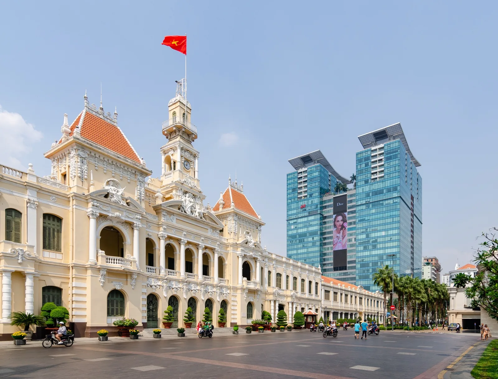 Ho Chi Minh City Hall's colonial facade contrasts with modern glass skyscrapers along the street beyond it.