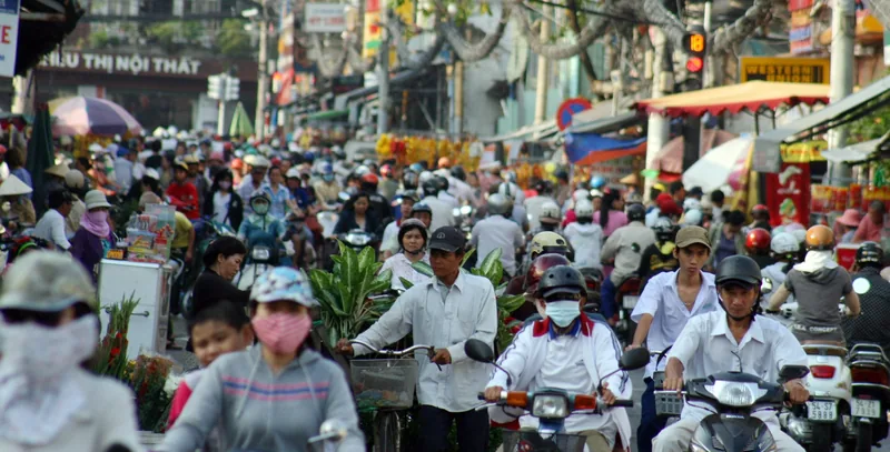 A dense crowd of motorbikes and pedestrians fills a busy street market in Ho Chi Minh City.