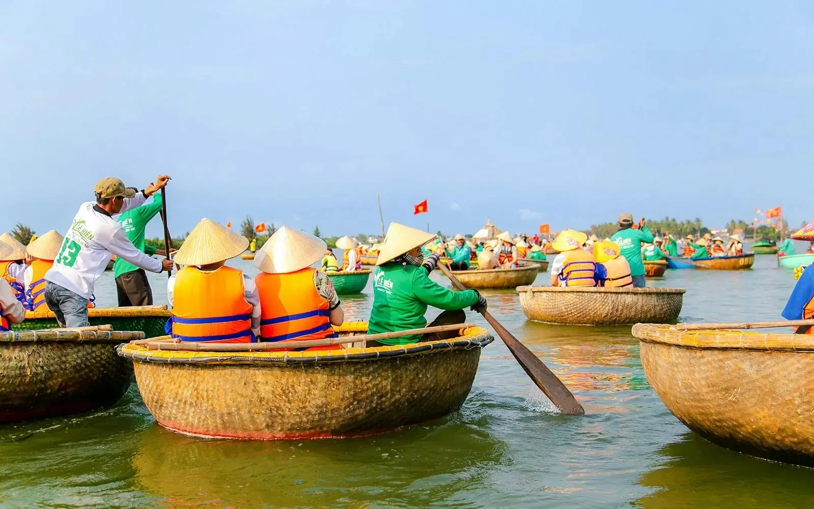 Tourists in life jackets ride round basket boats paddled by guides on the water at Cam Thanh, Hoi An.