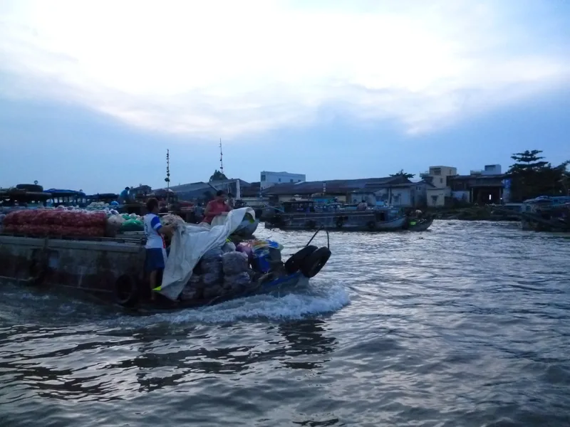 A cargo boat loaded with goods glides across the river at Cai Rang floating market near dusk in Can Tho.