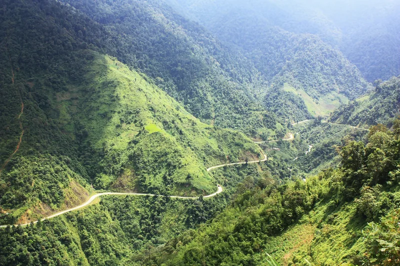 A winding mountain road cuts through lush green hills near Mu Cang Chai in Vietnam's northern highlands.