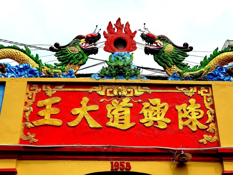 Twin green dragon sculptures flank a red and gold Chinese-lettered sign atop a temple building in Ho Chi Minh City.