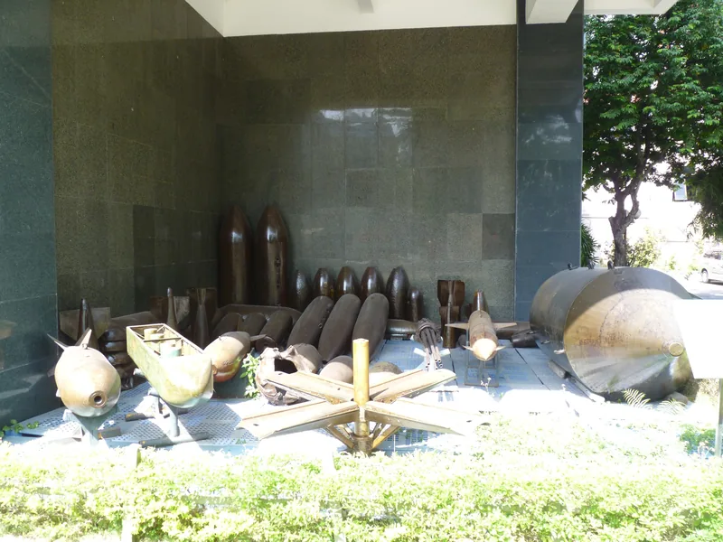 A row of old war-era bombs and shells displayed outdoors against a stone wall in Ho Chi Minh City.