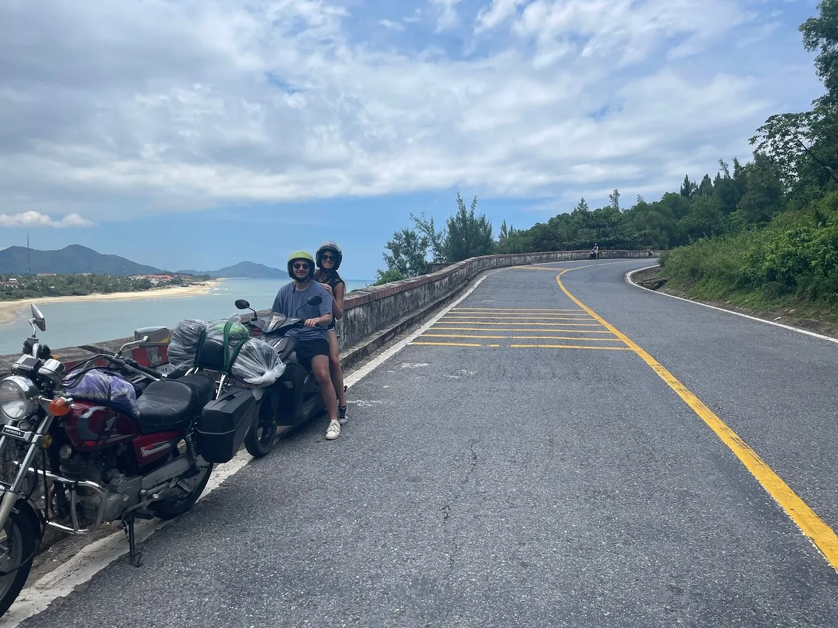 Two travelers pause on a loaded motorbike overlooking the coast along the winding Hai Van Pass.