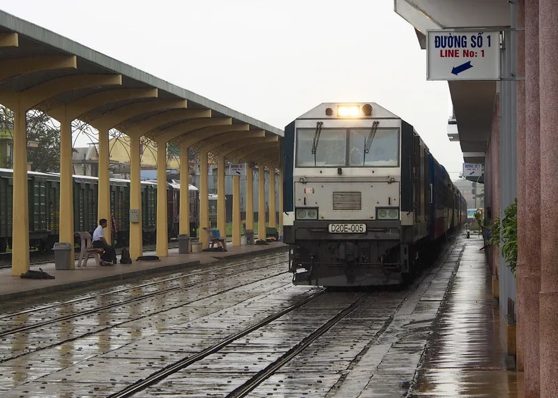 A diesel locomotive arrives at a rainy platform under a covered canopy at Hue railway station.