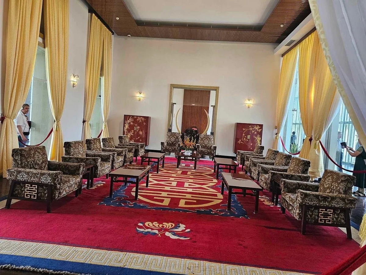 A formal reception hall with rows of upholstered armchairs on a red patterned carpet inside a Ho Chi Minh City palace.