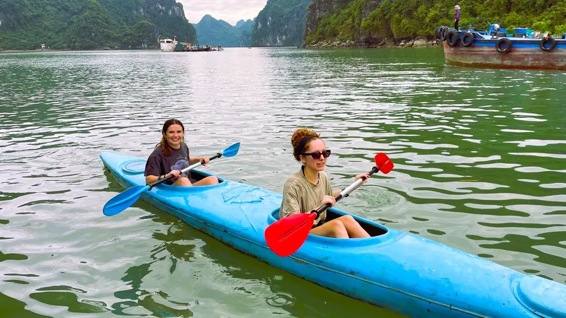 Two women paddle a blue kayak among limestone karsts on Lan Ha Bay near Cat Ba Island.