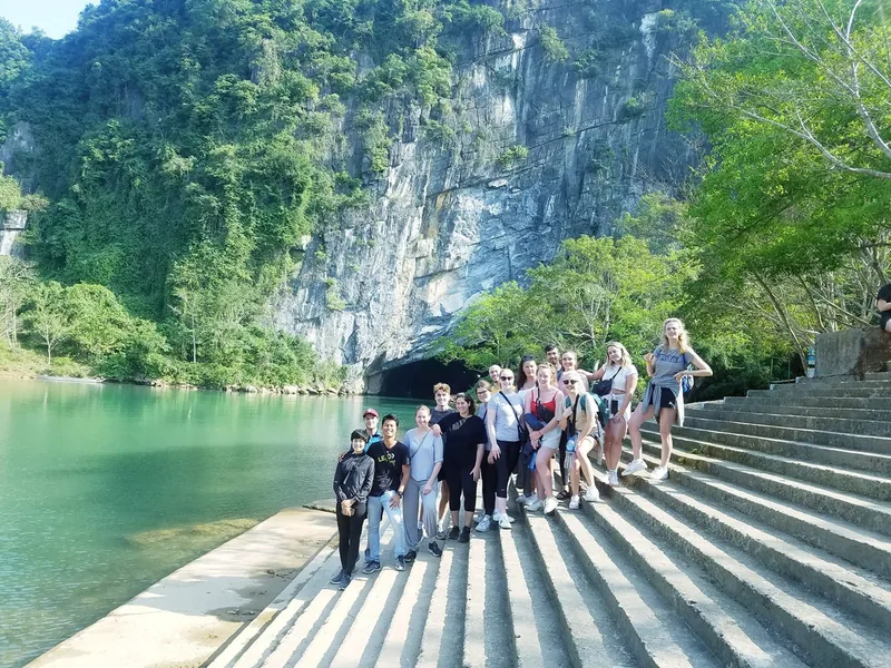 A group of tourists poses on steps beside a green river at the entrance to Paradise Cave in central Vietnam.