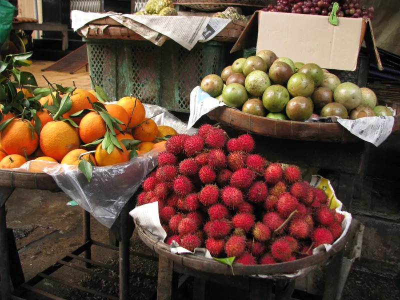 Baskets of rambutans, oranges, and green fruit displayed at a market stall in the Mekong Delta.