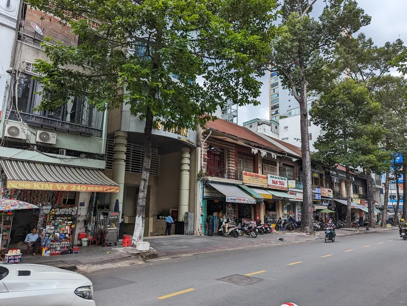 Tree-lined street with shophouses, storefront signs, and parked motorbikes in Ho Chi Minh City's District 1.