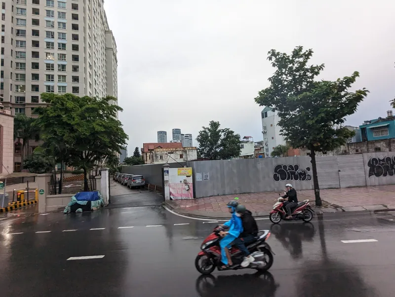 Motorbikes ride along a wet street lined with high-rise buildings and construction fencing in Ho Chi Minh City.