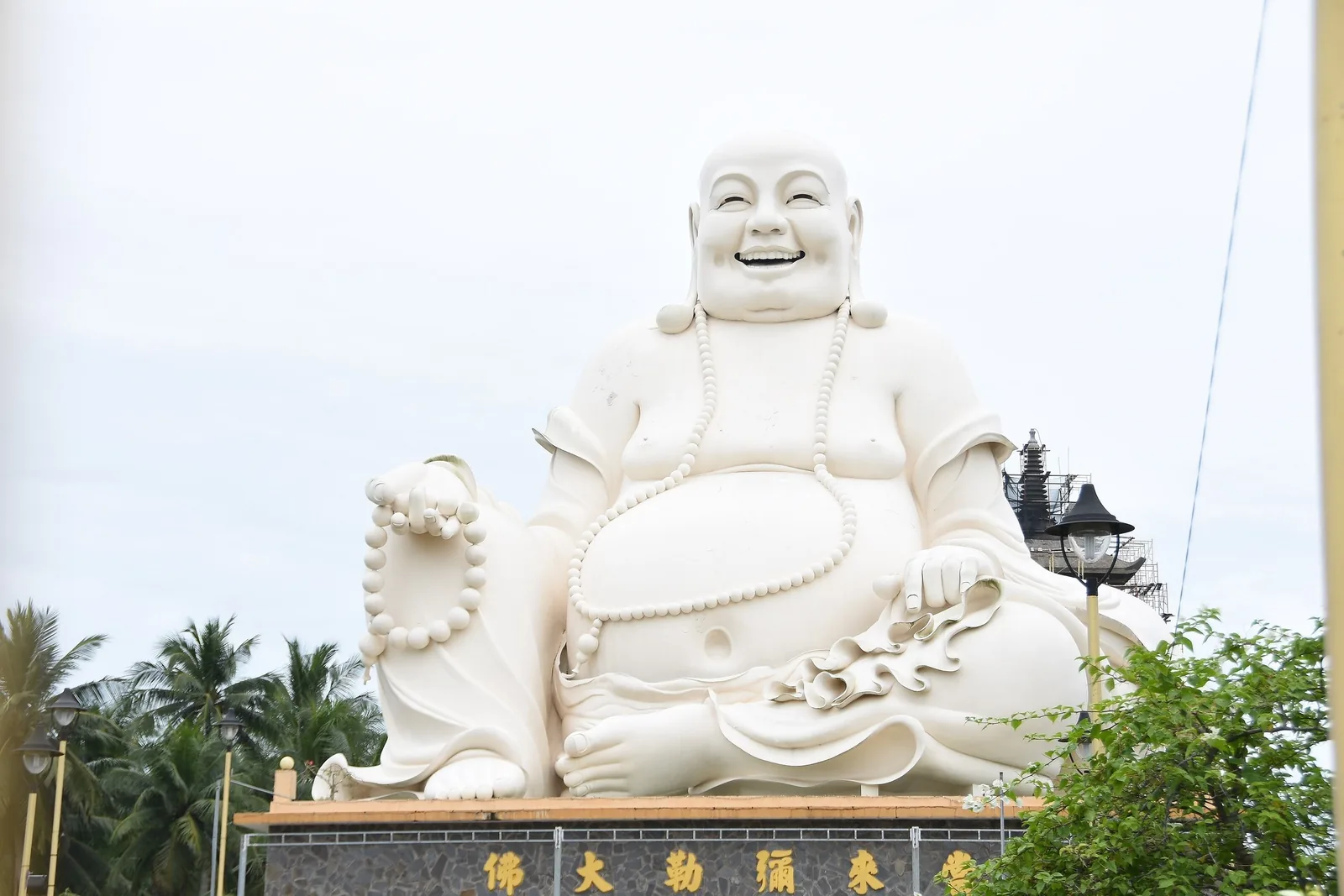 A giant white statue of the laughing Buddha sits atop a temple building in the Mekong Delta.