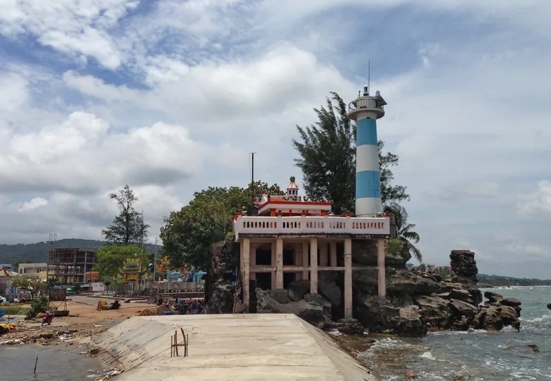 A blue-and-white lighthouse and small shrine sit on rocks above the sea at Dinh Cau, Phu Quoc.