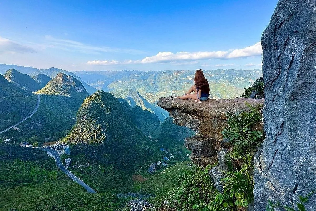 A woman sits on a rock ledge overlooking the winding mountain roads of the Ha Giang Loop.