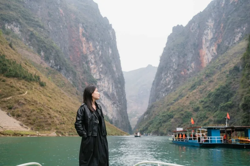 A woman stands on a boat deck admiring the towering limestone cliffs of the Nho Que River gorge in Ha Giang.