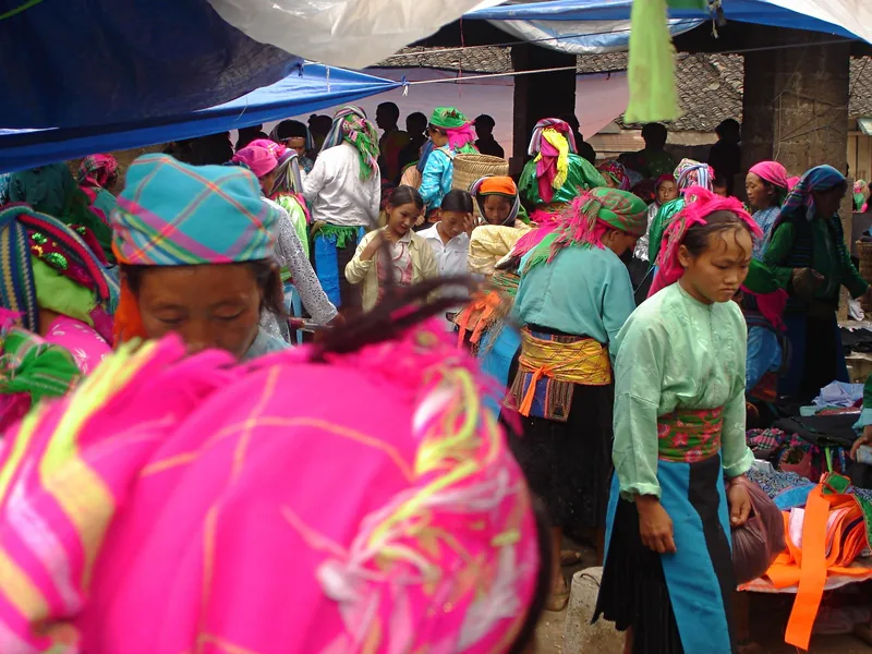 Ethnic minority women in vivid pink and green headscarves gather at a bustling market in Ha Giang.