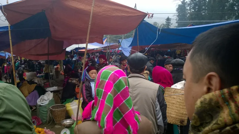 A crowded highland market in Ha Giang with tarp-covered stalls and Hmong shoppers in colorful traditional headscarves.