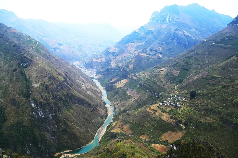 A turquoise river winds through the deep, terraced mountain canyon of Ha Giang, Vietnam.