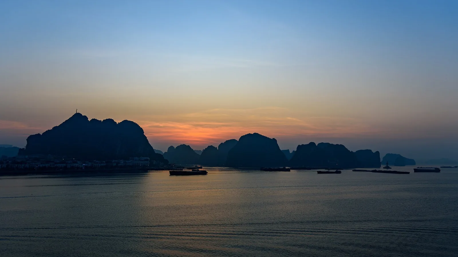 Silhouetted limestone karsts rise from calm waters at sunrise in Ha Long Bay, Vietnam.