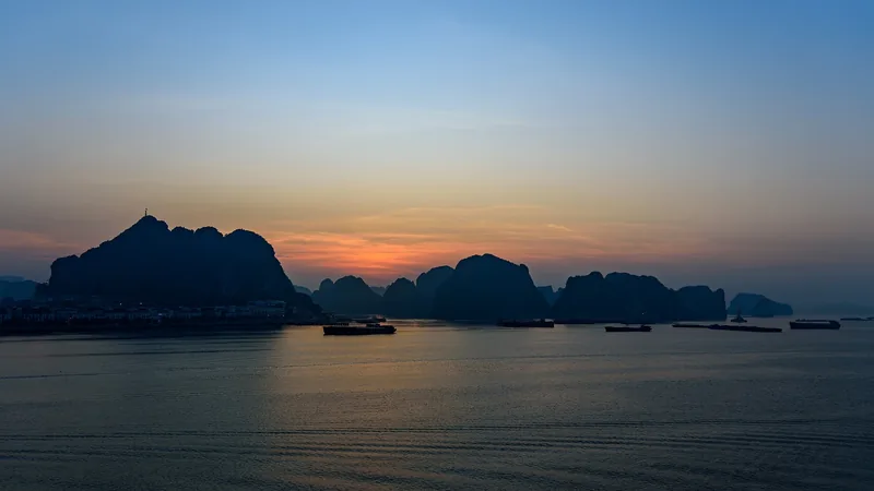 Silhouetted limestone karsts rise from calm waters at sunrise in Ha Long Bay, Vietnam.