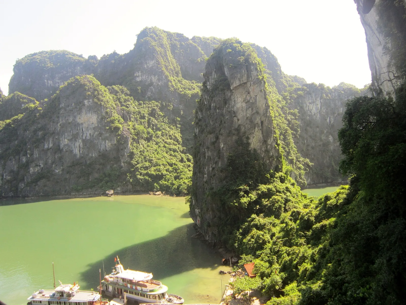 Limestone karsts rise above emerald water with cruise boats anchored below in Ha Long Bay.
