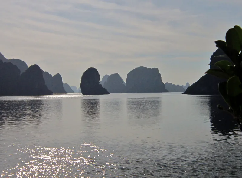 Silhouetted limestone karsts rise from the calm waters of Ha Long Bay at dawn.