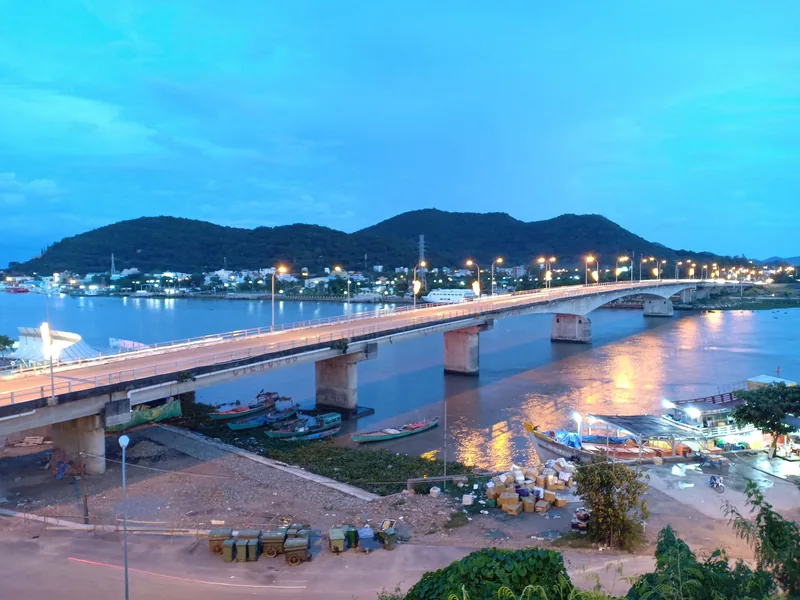 Twilight view of To Chau Bridge spanning a river with fishing boats and hills in Ha Tien, Vietnam.