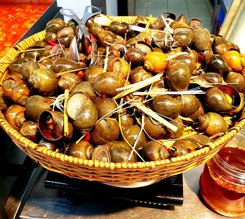 A woven basket piled with cooked snails and lemongrass, a popular Vietnamese street food dish.