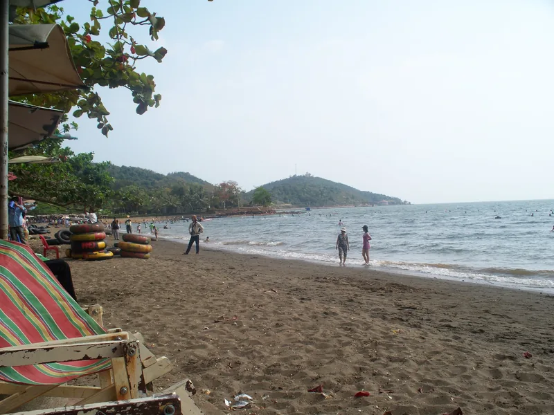 Beachgoers wade along a sandy shore with green hills in the distance at Mui Nai beach near Ha Tien.