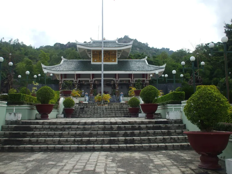 A memorial temple with curved tiled roofs and topiary plants sits at the top of stone steps in Chau Doc.