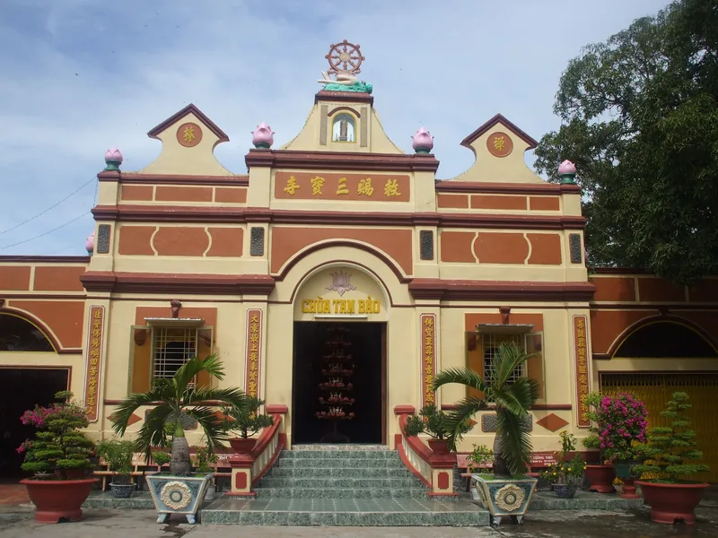 The ornate yellow facade of Chua Tam Bao pagoda in Ha Tien with potted bonsai plants lining the entrance steps.