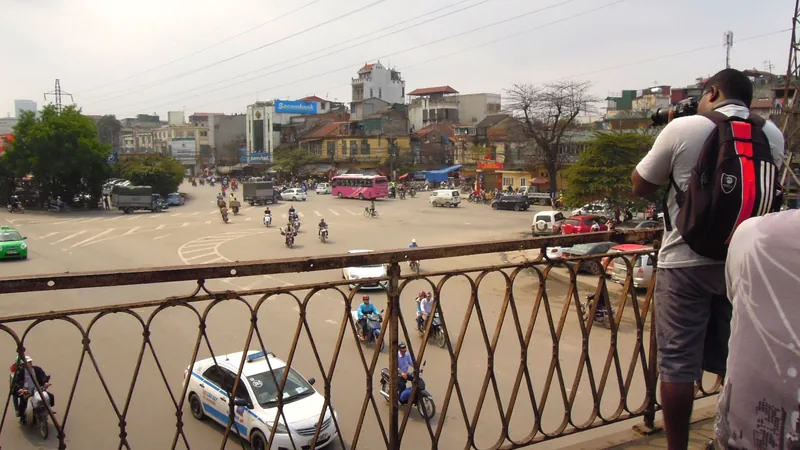 Traffic flows through a busy Hanoi intersection viewed from an ornate iron railing near Long Bien Bridge.