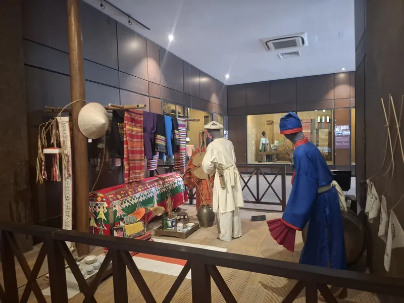 Museum display in Hanoi with mannequins in traditional dress and woven textiles from ethnic minority culture.