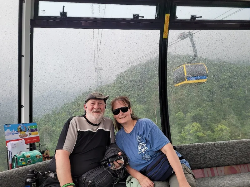 A couple smiles inside a rain-streaked cable car cabin overlooking forested mountains near Lao Cai.