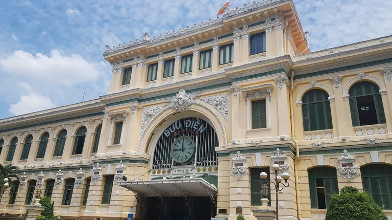 The colonial-era facade of the Saigon Central Post Office with its clock and arched windows under a blue sky.