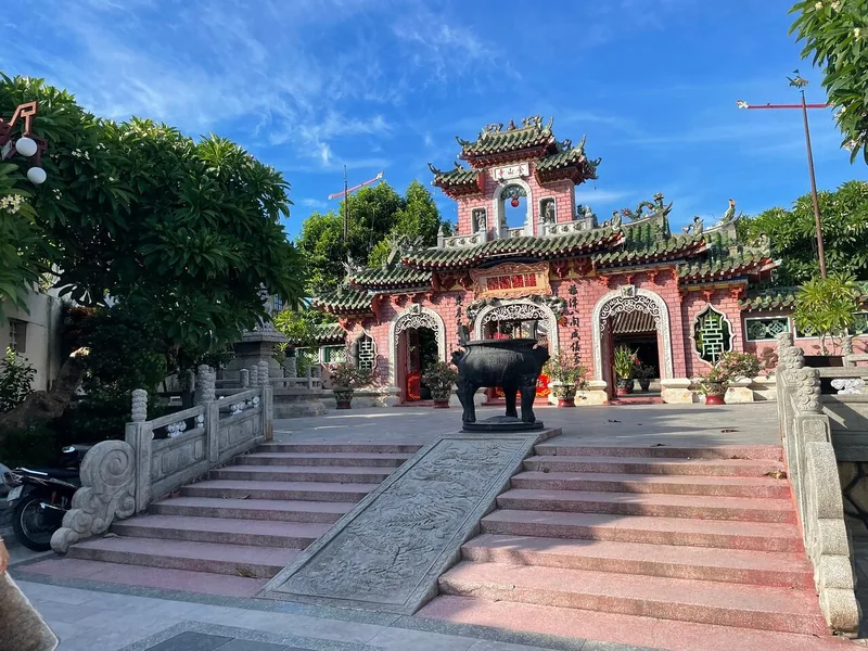 Ornate Chinese-style gate of a Hoi An assembly hall with a bronze incense burner and stone steps.