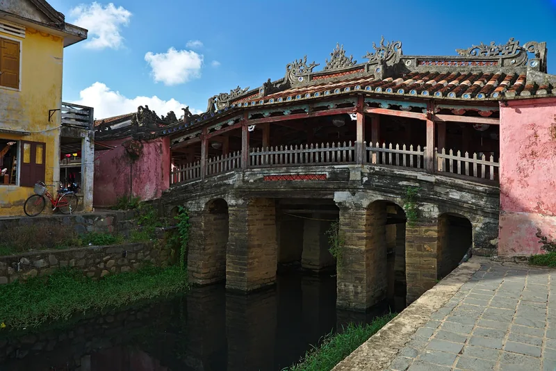 The historic covered Japanese Bridge with ornate tiled roof spans a narrow canal in Hoi An.