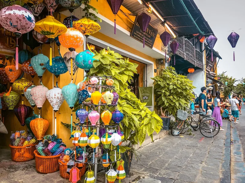 Colorful silk lanterns hang outside a shop on a yellow-walled street in Hoi An's old town.