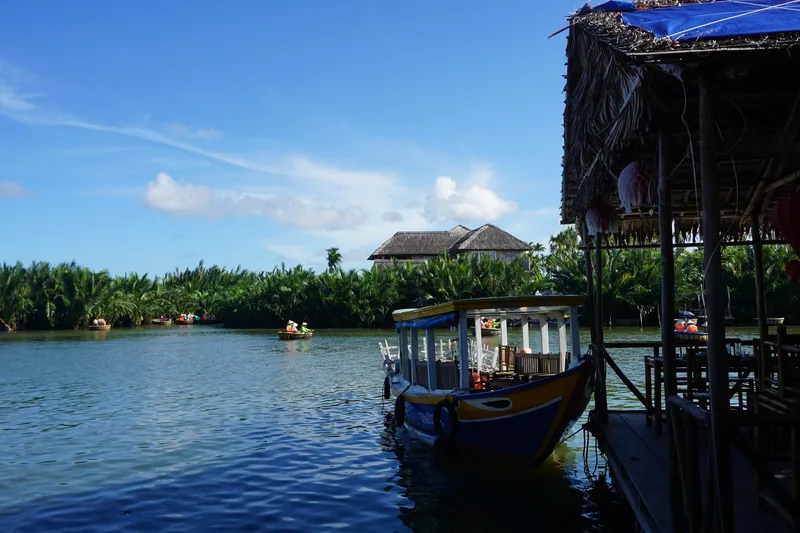 A tour boat docks beside a thatched hut on the coconut palm river near Hoi An.