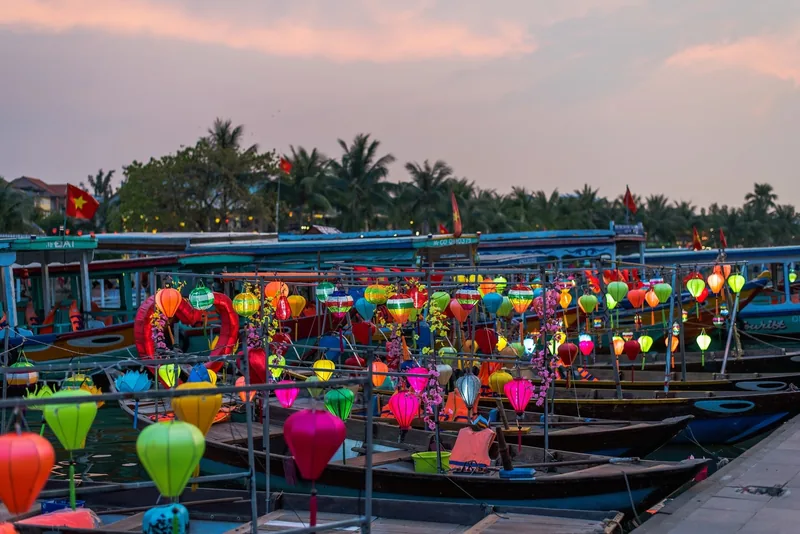 Colorful lanterns decorate wooden boats moored on the river at dusk in Hoi An.