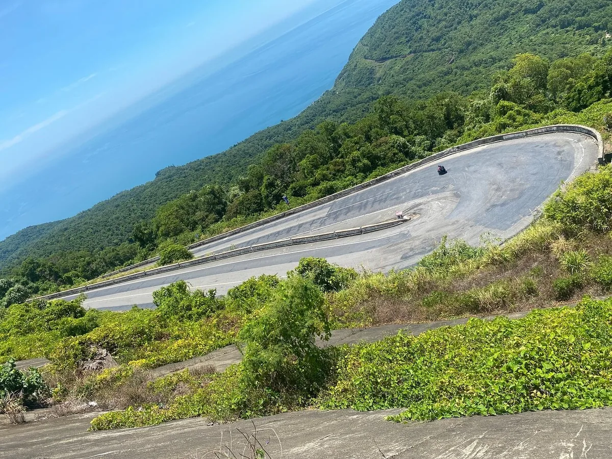 A hairpin bend winds down a forested mountainside above the sea on the road between Hue and Hoi An.