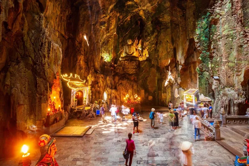 Visitors explore a sunlit cave temple with shrines inside Marble Mountain, Da Nang.