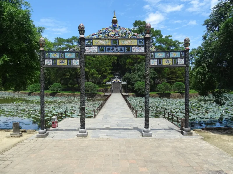 An ornate mosaic gate leads across a lotus pond bridge at Minh Mang Tomb in Hue.