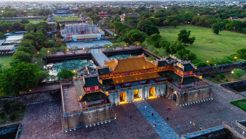 Aerial view of Hue Imperial City's illuminated gate and moat at dusk, surrounded by green parkland.