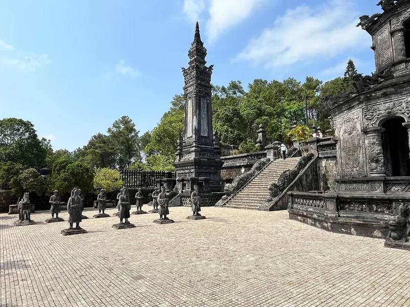 Stone mandarin statues line the courtyard of Khai Dinh Tomb in Hue under a tall obelisk and ornate stairway.