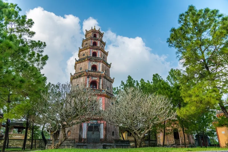 The seven-story Thien Mu Pagoda tower rises above trees under a blue sky in Hue.