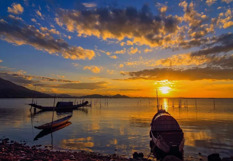 Wooden fishing boats rest on the calm water of Tam Giang Lagoon under a vivid orange sunset sky.