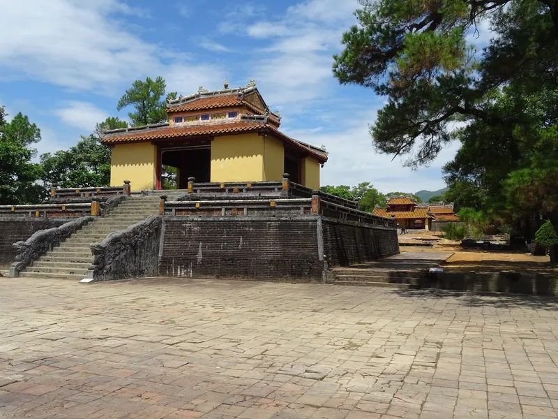 A yellow pavilion with a tiled roof stands atop stone steps at the Mausoleum of Emperor Minh Mang in Hue.