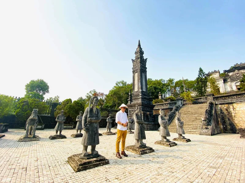 A visitor in a conical hat stands among stone mandarin statues at Khai Dinh Tomb's courtyard in Hue.