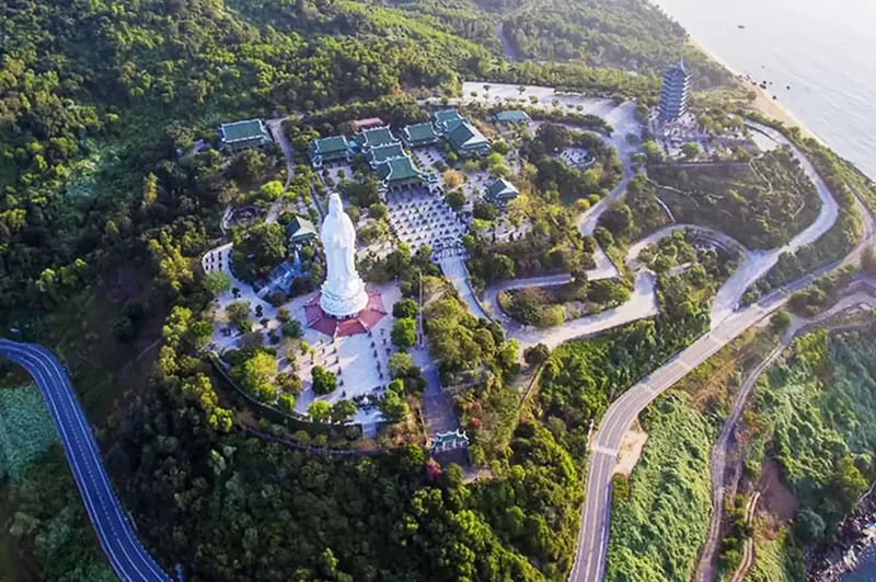 Aerial view of Linh Ung Pagoda's white Lady Buddha statue amid green forested hills near the coast in Da Nang.